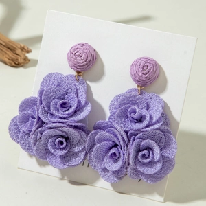 Detailed shot of purple fabric rose earrings with hand-woven beads on white card
