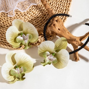 Détail macro du collier orchidée aux pétales crème et perles sur décor en bois