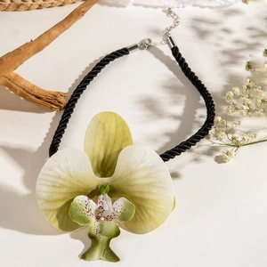 Gros plan d'un collier avec pendentif orchidée aux nuances violettes sur un fond naturel