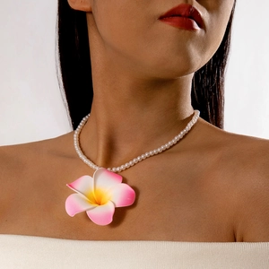 Gros plan d'un pendentif fleur de frangipanier sur un collier de perles porté par un modèle