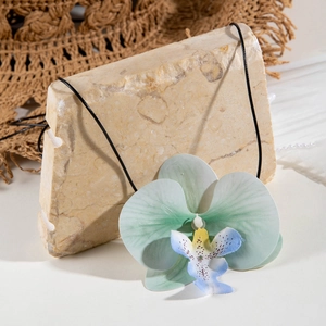 Détail du pendentif orchidée bleu-vert avec cordon noir sur une surface en pierre