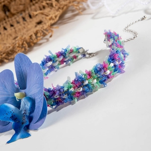 Détail d'un collier bohème à pompons colorés avec perles et accent floral d'orchidée