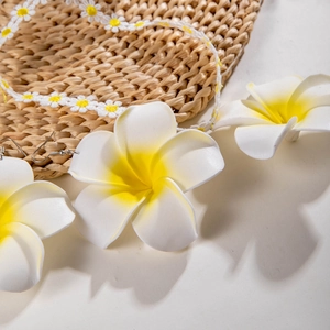 Détail de boucles d'oreilles frangipanier et collier marguerite sur chapeau de paille