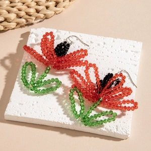 Close-up of handmade flower beaded earrings with red petals and green leaves on stone