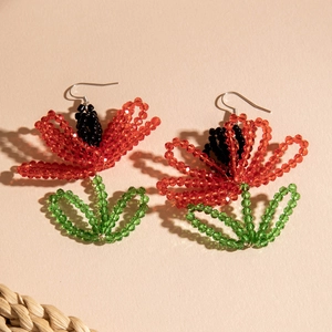 Macro shot of handmade beaded poppy earrings with red petals and green leaf details