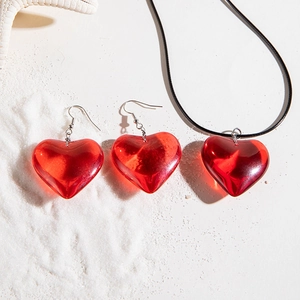 Macro shot of red heart jewelry set with earrings and necklace on white sand backdrop