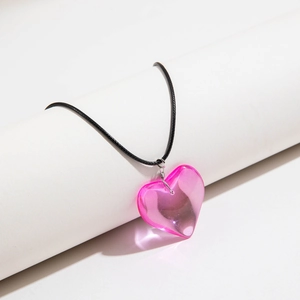 Close-up of translucent pink heart pendant on black cord hanging on a white cylinder