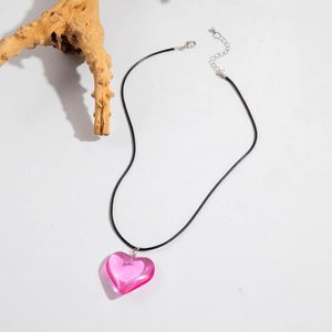 Detailed close-up of a pink resin heart pendant on a black cord necklace over white background