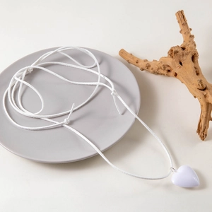 Detail of adjustable white cord necklace featuring a polished heart pendant on a grey plate