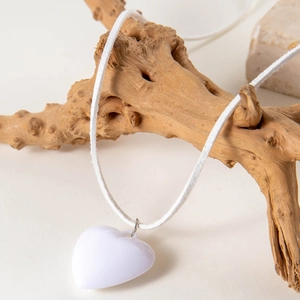 Close-up of white heart pendant on cord necklace displayed on natural wooden branch