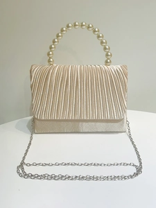 Detail of champagne satin evening bag with pleated texture and round pearl handle