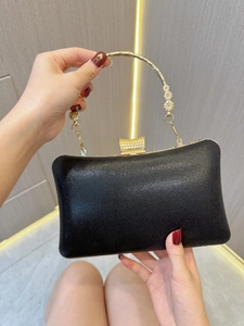 Detail of elegant black satin evening bag with decorative gold floral handle and clasp