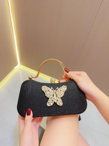 Detailed close-up of a black glitter evening clutch with a luxury rhinestone bow and gold handle