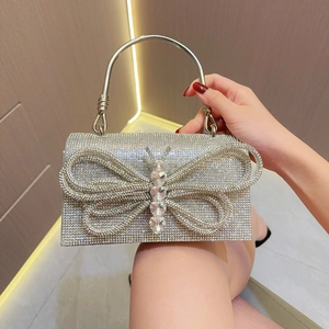 Detalle del bolso de noche plateado con pedrería, mariposa de cristal y asa metálica redonda