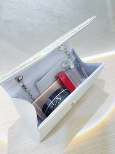 White pearl evening clutch with rhinestones and metal chain on a wood table