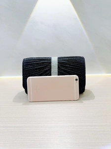 Detail of a black pleated clutch bag with silver rhinestones compared to a smartphone