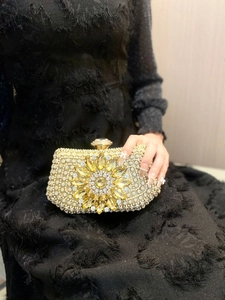 Close-up of luxury gold evening clutch with crystal floral brooch on black dress