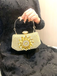 Detail of a luxury gold evening clutch with crystal sunflower pattern and metal handle