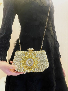 Close-up of golden sunflower evening bag with crystals on a black fringe dress