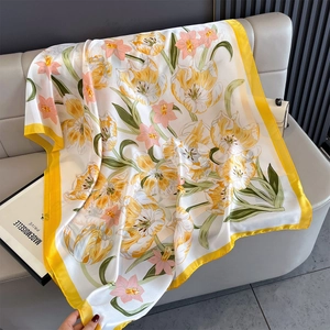 Close-up of silk scarf with yellow tulips and pink flowers draped on a grey sofa