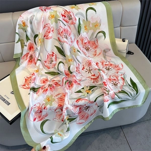 Detail shot of silk-feel scarf with red tulips and green borders on a leather sofa