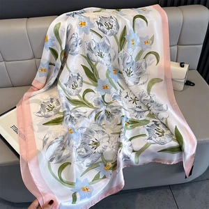 Close-up of lightweight silk satin beach shawl with tulip floral print on a leather sofa