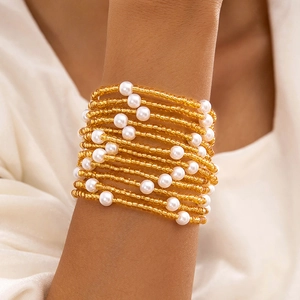 Détail d'un bracelet multi-rangs avec perles dorées et perles nacrées blanches sur poignet