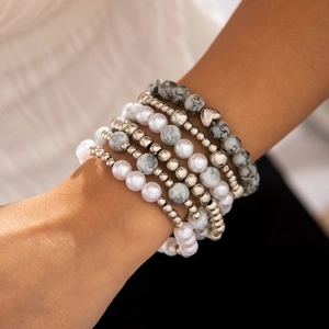 Détail d'un ensemble de bracelets multicouches avec perles et breloque coeur au poignet