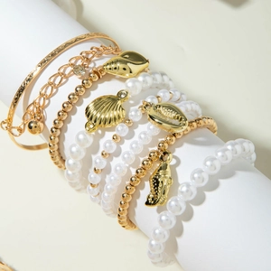 Détail de bracelets multicouches à pendentifs coquillages dorés et perles blanches