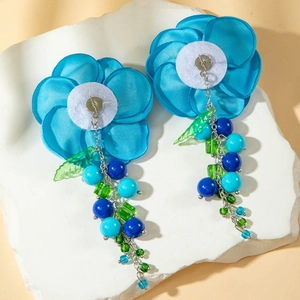 Dettaglio di orecchini a fiore in seta blu con nappe di perline su fondo di pietra