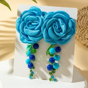Dettaglio di orecchini a fiore in raso blu con frange di perline su carta bianca