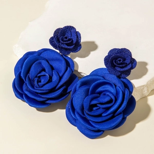 Dettaglio degli orecchini a rosa in tessuto blu reale su sfondo di pietra bianca