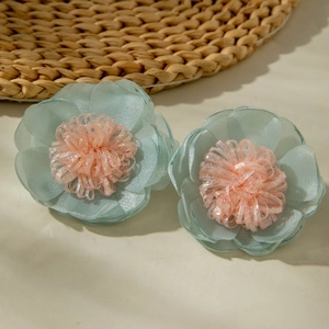 Dettaglio di orecchini a fiore in organza azzurra con stami viola scintillanti e texture