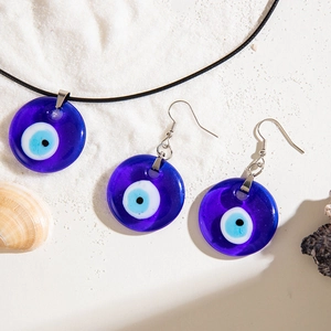 Detail of cobalt blue glass evil eye pendant necklace and earrings on white sand beach