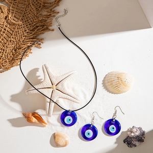 Blue glass evil eye jewelry set displayed on beach sand with starfish and shells