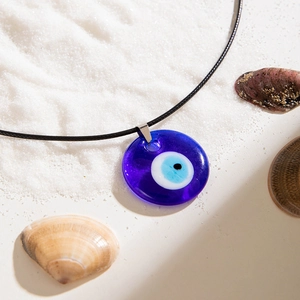 Blue glass evil eye pendant on black woven rope over beach sand and shells