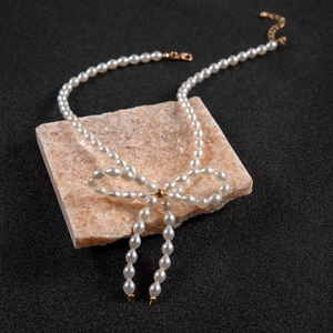 Elegant white pearl necklace featuring a golden bow pendant on a pink stone background