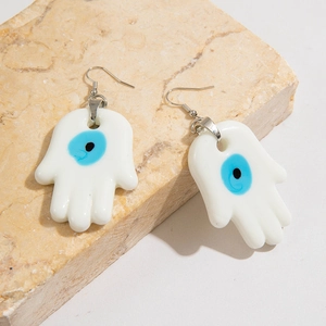 Detailed view of Hamsa Hand earrings with blue evil eye on natural stone background