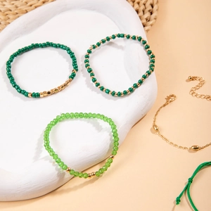 Détail des perles vertes et breloques dorées sur des bracelets bohèmes empilés