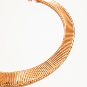 Close-up of rose gold textured metal collar necklace with intricate ribbed geometric design