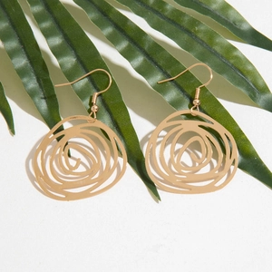 Detailed close-up of golden irregular openwork rose earrings on a green leaf background