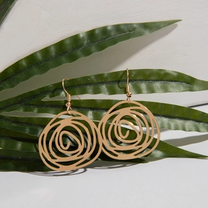 Detailed shot of gold-plated irregular spiral rose earrings hanging on a green leaf