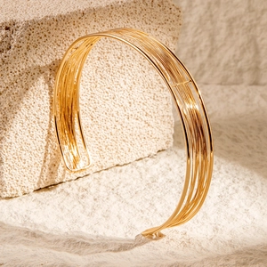 Detail of a minimalist multi-layered gold open cuff bracelet on stone background