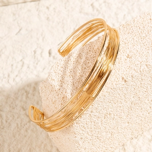 Detail of minimalist gold multi-strand wire cuff bracelet on textured white stone