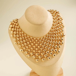 Close-up of a multi-layer golden bead statement necklace with a modern grid-like design