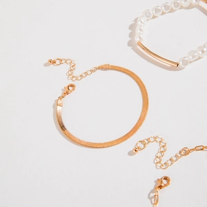 Detailed view of gold snake chain and pearl tube bracelets set on a neutral background