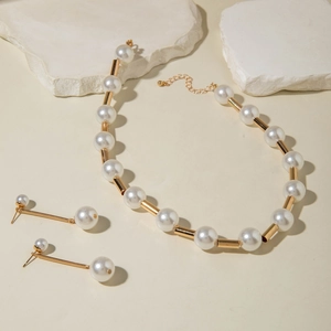 Macro view of large white faux pearls and gold cylindrical tube links on the jewelry set