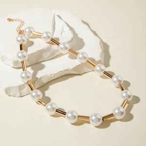 Detail of faux pearl necklace with gold cylinders on white stones and warm beige background