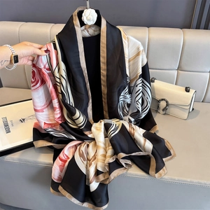 Black silk satin shawl with pink floral print and golden wavy lines on a display hanger