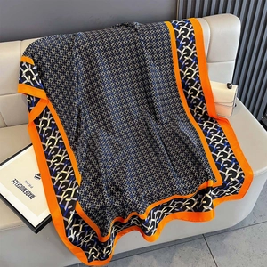 Detail of silk scarf with geometric pattern and orange border draped on a sofa